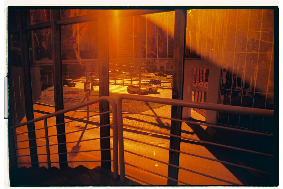 Sunlight through a stairwell window onto a city street, seen from inside a building.